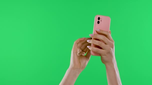 Жіночі руки тримають смартфон вертикально на тлі зеленого екрану ключа хроми. Руки торкаються сенсорного екрана, вводять текст або повідомлення, прокручують його. Повільний рух. крупним планом . — стокове відео