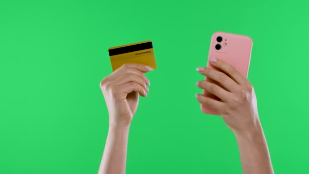 Vrouwelijke handen houden een creditcard en een smartphone tegen de achtergrond van een groen scherm van een chroma sleutel. Een smartphone gebruiken voor aankopen en betalingen via internet met een creditcard. Sluiten.. — Stockvideo