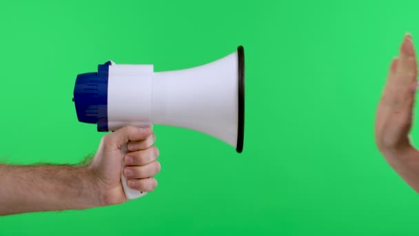 Uma mão de homem está segurando um megafone branco e uma mão de mulher está fazendo um sinal de parada contra o fundo da tela verde da tecla chroma. Um anúncio, um anúncio. Movimento lento. Fechar. — Vídeo de Stock