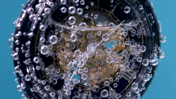 Orologio d'epoca su una catena ricoperta di bolle d'aria in acqua trasparente su fondo blu. Primo piano del quadrante dell'orologio. Rallentatore. — Video Stock