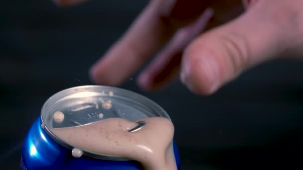 Opening a shaken blue can of beer, cola, from which a frothy drink is poured. A detailed shot of a mans hand opening a stirred beer can against a black background. Slow motion. Close up. — Stock Video