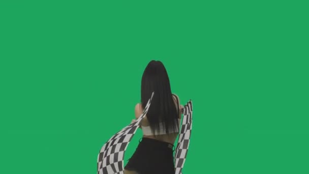 Achteraanzicht van sexy brunette in korte broek zwaaiend met zwart-wit geblokte race vlaggen. Jonge vrouw poseren tegen de achtergrond van groen scherm in studio close-up. Slow motion klaar, 4K bij 59,94fps. — Stockvideo