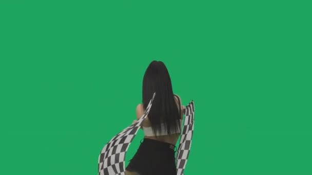 Visão traseira da morena sexy em shorts curtos acenando bandeiras de corrida quadriculadas em preto e branco. Jovem posando contra fundo de tela verde em estúdio de perto. Movimento lento pronto, 4K a 59.94fps. — Vídeo de Stock