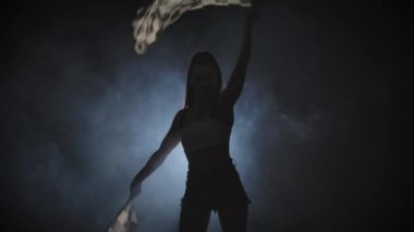 İnce, genç bir bayrağın gölgesi bir yarış yarışının başladığını işaret etmek için damalı bayrak sallıyor. Esmer, arka ışıklandırmalı dumanlı bir stüdyoda poz veriyor. Kapatın. Yavaş çekim hazır, 4K 59.94fps 'de..