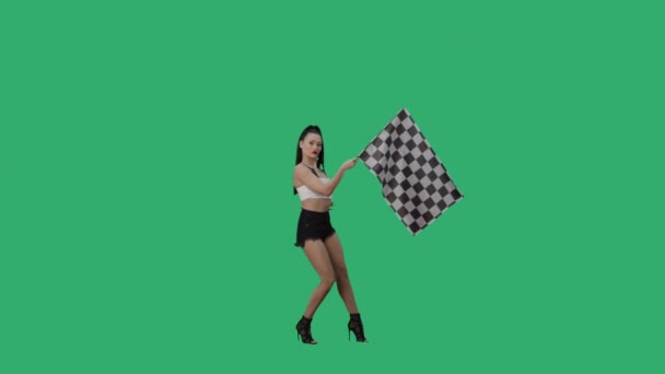 Sexy morena ondeando bandera de carreras a cuadros en blanco y negro para señalar el inicio de la competencia. Mujer joven posando de cuerpo entero sobre fondo de pantalla verde. Cámara lenta lista, 4K a 59.94fps — Vídeo de stock