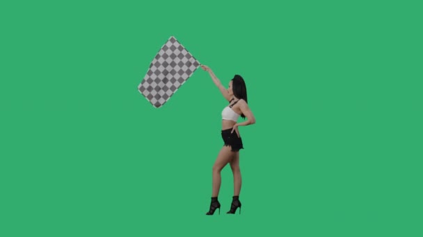 Zijaanzicht van brunette zwaaiend zwart-wit geruite race vlag om het begin van de concurrentie aan te geven. Jonge vrouw poseren volledige lengte tegen de achtergrond van groen scherm. Slow motion klaar, 4K bij 59,94fps. — Stockvideo