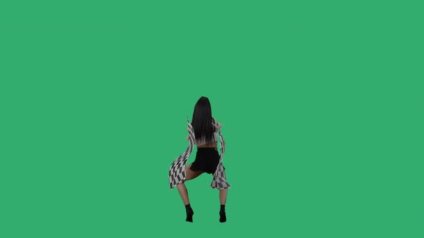 Achteraanzicht van sexy brunette in korte broek zwaaiend met zwart-wit geblokte race vlaggen. Jonge vrouw poseren volledige lengte tegen de achtergrond van groen scherm in de studio. Slow motion klaar, 4K bij 59,94fps — Stockvideo