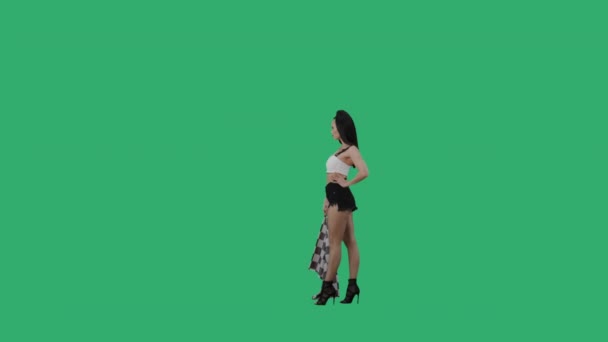 Side view of brunette waving black and white checkered racing flag to signal start of competition. Young woman posing full length against background of green screen. Slow motion ready, 4K at 59.94fps. — Stock Video