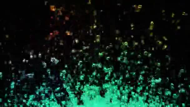 Färgade droppar vatten flyger upp och spraya i olika riktningar på svart bakgrund. Makro skott av transparent vätska som skapar droppar och stänk som orsakas av ljudvibrationer. Sakta i backarna. Närbild. — Stockvideo
