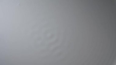 Titreşim tarafından uyarıldığında beyaz yüzey süt sıvısının dalga hareketi. Dalgaların doğasındaki değişimler ve sütün yüzeyindeki dalgalanma ve heyecan verici titreşimlerdeki değişim. Ağır çekim. Kapat..