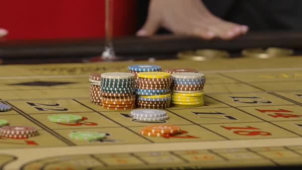 Male croupier collects the chips laid out on the roulette table. In the background, a blurred view of a woman in a red drinking champagne from glass. Hands close up. Slow motion ready, 4K at 59.94fps. — Stock Video