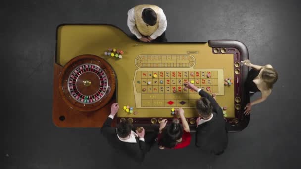 Верхний вид группы мужчин и женщин, делающих ставки с фишками на игровой рулетке в казино. Ставка выигрывает, а крупье отдает выигрыш счастливчику. Медленное движение готово, 4K на 59,94fps. — стоковое видео