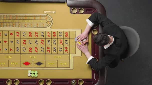 髭の男のトップビューは、カジノでギャンブルルーレットテーブルに座って賭け、すべてのチップを危険にさらしています。ベットは失われ、プレイヤーは動揺しています。桟橋はすべてのチップを取ります。スローモーション準備完了、 59.94fpsで4K. — ストック動画