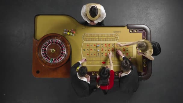 Vue du dessus d'un groupe d'hommes et de femmes pariant avec des jetons sur une table de roulette de jeu dans un casino. Les paris sont perdus et le croupier revendeur prend tous les jetons. Prêt au ralenti, 4K à 59.94fps. — Video