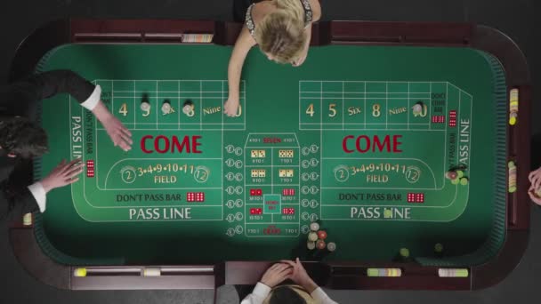 Vue de dessus de deux hommes et d'une femme jouant au craps assis à une table dans un casino. Les joueurs placent des paris avec des jetons. L'homme lance les dés et gagne. Prêt au ralenti, 4K à 59.94fps. — Video