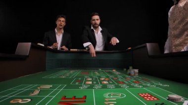 Kumarhanedeki yeşil barbut masasında duran takım elbiseli iki adam. Oyuncu zar atar ve kazanır. Erkekler sevinçle sevinir ve duyguları hayrete düşürürler. Oyun masasının içinden bak. Yavaş çekim.