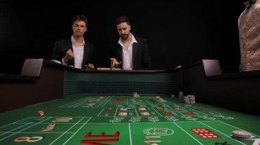 Kumarhanedeki yeşil barbut masasında duran takım elbiseli iki adam. Oyuncu zar atar ve kaybeder. Erkekler çok üzgün ve hayal kırıklığına uğramış. Oyun masasının içinden bak. Yavaş çekim.