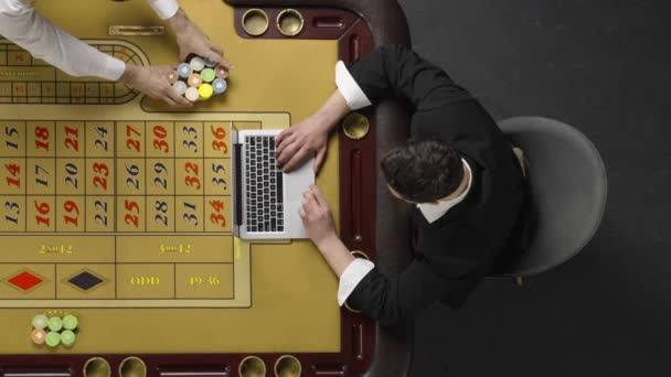 Κάτοψη του γενειοφόρου άνδρα που κάθεται στο τραπέζι της ρουλέτας και παίζει σε ένα online καζίνο στο laptop. Ο κύριος κερδίζει και γιορτάζει τη νίκη. Βροχή χρημάτων. Αργή κίνηση έτοιμη, 4K στα 59.94fps. — Αρχείο Βίντεο