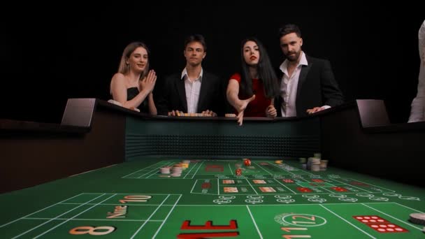 Eine Gruppe Männer und Frauen steht an einem grünen Würfelspieltisch. Die Dame im roten Kleid würfelt und verliert. Das Unternehmen ist sehr verärgert. Blick von innen auf den Spieltisch. Zeitlupe. — Stockvideo