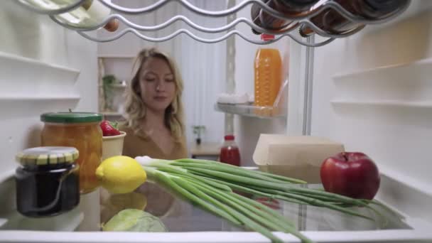 Genç bir kadın buzdolabının kapısını açar ve hamburger kutusuyla meyve suyunu çıkarır. Aç sarışın kız akşam yemeği yemek üzere. Buzdolabının içinden bak. Kapatın. Yavaş çekim hazır 59.94fps. — Stok video