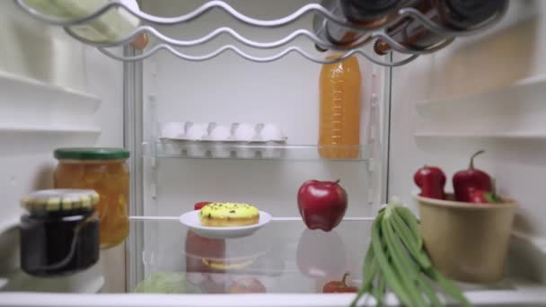 Beautiful young woman opens the refrigerator door, looks inside, happy takes out a cake instead of an apple. View from inside the kitchen fridge. Close up. Slow motion ready 59.94fps. — 图库视频影像