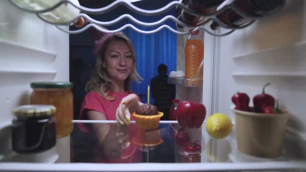 Happy young woman at night, takes out cupcake with candle from refrigerator. Blonde lights candle and wishes her boyfriend happy birthday. View from inside fridge. Close up. Slow motion ready 59.94fps — 비디오