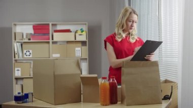 Depo çalışanı bir ofis odasında kutuların arka planına karşı çalışıyor. Kadın müşterilere teslimat için paketler hazırlıyor. Kapatın. Yavaş çekim hazır 59.94fps.