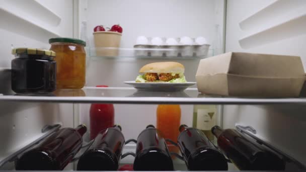 Mujer joven abre la puerta del refrigerador por la noche, mira dentro y feliz saca dos botellas de cerveza. Vista desde el interior de la nevera de la cocina. De cerca. Cámara lenta lista 59.94fps. — Vídeo de stock