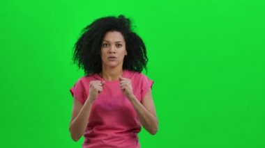 Genç Afro-Amerikan kadın portresi. Heyecan ve heyecanla kameraya bakıyor, sonra da çok üzgün. Kıvırcık saçlı siyah kadın yeşil ekranda poz veriyor. Kapatın. Yavaş çekim hazır 59.97fps.