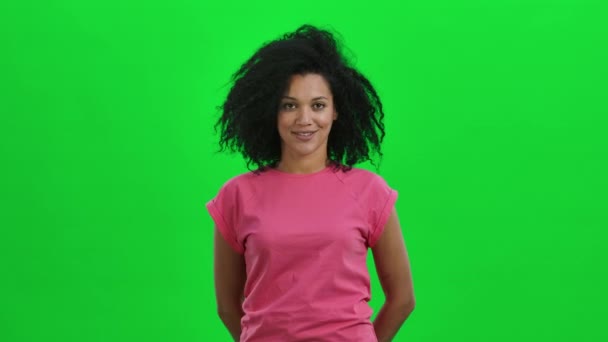 Portrét mladé Afroameričanky přikyvuje a ukazuje na to, aby to nedělala gestem. Černá žena s kudrnatými vlasy pózuje na zelené obrazovce ve studiu. Zavřít. Zpomalení připraveno 59.97fps.