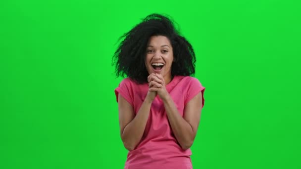 Portret młodej Afroamerykanki patrzącej w kamerę z zachwytem i radością. Czarna kobieta z kręconymi włosami pozuje w studio na zielonym ekranie. Zamknij drzwi. Wolny ruch gotowy 59.97fps. — Wideo stockowe