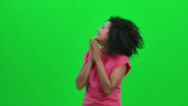 Retrato de una joven afroamericana que mira a su alrededor con alegría y ternura. Mujer negra con el pelo rizado posa en la pantalla verde en el estudio. De cerca. Cámara lenta lista 59.97fps. — Vídeo de stock