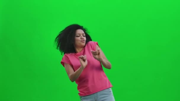 Retrato de una joven afroamericana bailando alegremente la danza de la victoria, la alegría o el buen humor. Mujer negra con el pelo rizado posa en pantalla verde en el estudio. De cerca. Cámara lenta lista 59.97fps. — Vídeo de stock