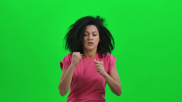 Retrato de una joven afroamericana mirando a la cámara con emoción, luego celebrando su triunfo de victoria. Mujer negra posa en pantalla verde. De cerca. Cámara lenta lista 59.97fps. — Vídeo de stock