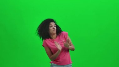 Genç Afro-Amerikan kadın portresi neşeyle dans ediyor zafer dansı, neşe ya da iyi ruh hali. Kıvırcık saçlı siyah kadın stüdyoda yeşil ekranda poz veriyor. Kapatın. Yavaş çekim hazır 59.97fps.