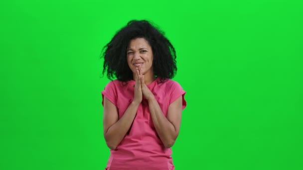 Retrato de una joven afroamericana manteniendo la palma unida y pidiendo algo. Mujer negra con el pelo rizado posa en la pantalla verde en el estudio. De cerca. Cámara lenta lista 59.97fps. — Vídeo de stock