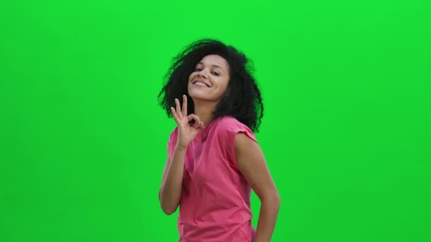 Retrato de una joven afroamericana sonriendo y haciendo un cartel bien. Mujer negra con el pelo rizado posa en la pantalla verde en el estudio. De cerca. Cámara lenta lista 59.97fps. — Vídeo de stock