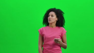Doğru yere gitmek için akıllı telefondan haritaya bakan genç Afrikalı Amerikalı kadın portresi. Kıvırcık saçlı siyah kadın stüdyoda yeşil ekranda poz veriyor. Kapatın. Yavaş çekim hazır 59.97fps.