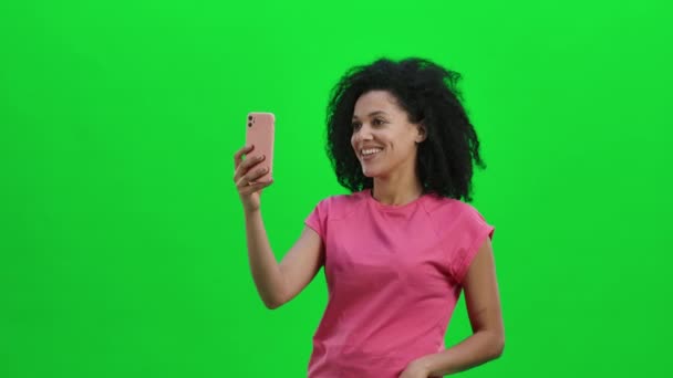 Retrato de una joven afroamericana hablando por video chat usando el teléfono móvil y regocijarse. Mujer negra con el pelo rizado posa en la pantalla verde en el estudio. De cerca. Cámara lenta lista 59.97fps. — Vídeo de stock