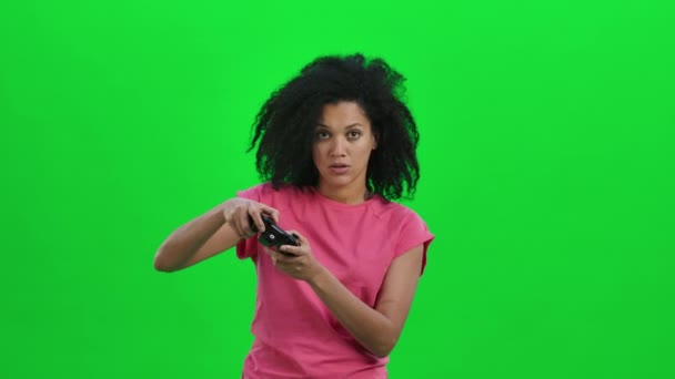 Portrait de jeune Afro-Américaine jouant à un jeu vidéo à l'aide d'une manette sans fil. Femme noire aux cheveux bouclés pose sur écran vert dans le studio. Ferme là. Ralenti prêt 59.97fps. — Video