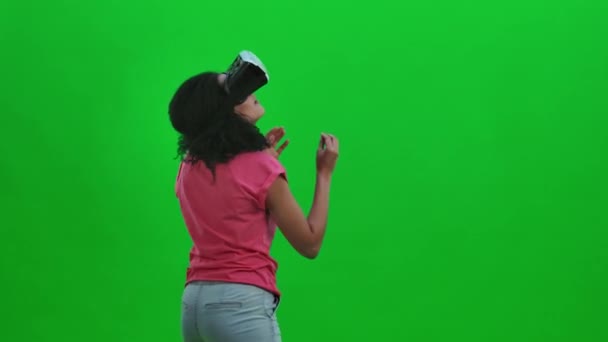 Retrato de una joven afroamericana con auriculares de realidad virtual o gafas 3D. Mujer negra con el pelo rizado posa en la pantalla verde en el estudio. De cerca. Cámara lenta lista 59.97fps. — Vídeo de stock