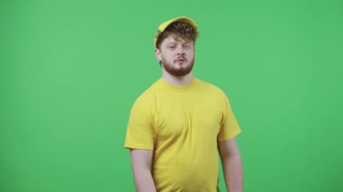 Kameraya bakıp omzuna termo torba takan gençlerin portresi. Sarı kurye üniformalı kızıl saçlı erkek stüdyoda yeşil ekranda poz veriyor. Kapatın. Yavaş çekim hazır 59.97fps.