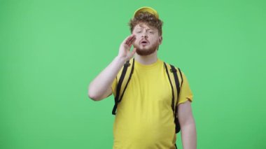 Birilerini çağıran genç adamların portresi. Sarı kurye üniformalı kızıl saçlı erkek. Stüdyoda yeşil ekranda termo çantalı poz veriyor. Kapatın. Yavaş çekim hazır 59.97fps.