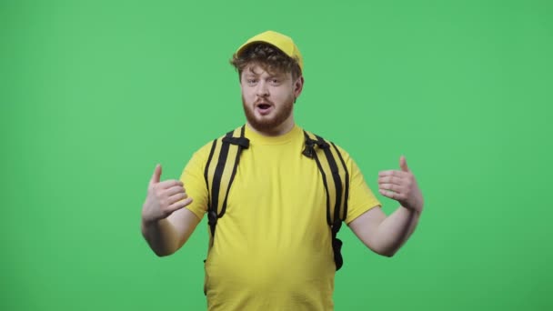 Portrait of young men telling information and gesturing with his hands. Redhead male in yellow delivery courier uniform with thermo bag posing on green screen. Close up. Slow motion ready 59.97fps. — Stock Video