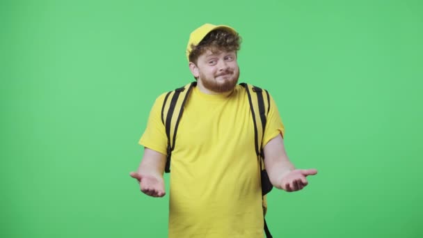 Retrato de homens jovens encolhendo os ombros, suspirando e joga as mãos para cima. Macho ruivo em uniforme de estafeta de entrega amarela com bolsa térmica posando na tela verde em estúdio. Fecha. Movimento lento pronto 59.97fps — Vídeo de Stock