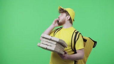 Telefonda konuşan genç erkeklerin portresi pizza kutusunu düşürüyor ve çok üzgün. Sarı kurye üniformalı, yeşil ekranda duran termo çantalı kızıl saçlı erkek. Kapatın. Yavaş çekim hazır 59.97fps.