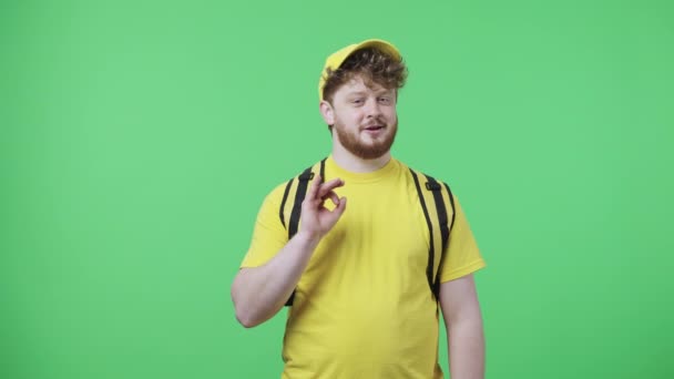 Портрет молодых людей, делающих знак ОК. Рыжий мужчина в желтой курьерской форме с термомешком позирует на зеленом экране в студии. Закрывай. Готовность к медленному движению 59,97fps. — стоковое видео