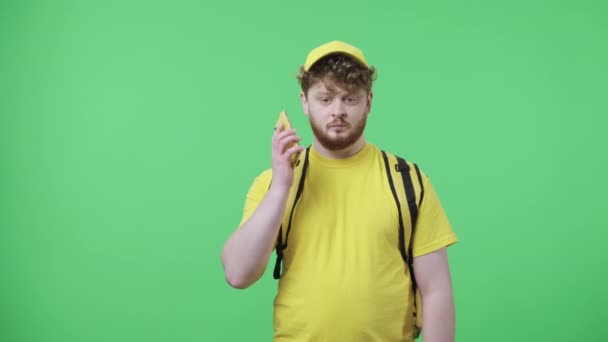Portret van jonge mannen die praten voor mobiele telefoon. Roodharige man in gele koerier uniform met thermo tas poseren op groen scherm in de studio. Sluit maar af. Slow motion klaar 59,97 fps. — Stockvideo