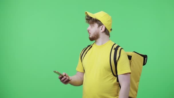 Portret van jonge mannen die telefoneren, met een afleveradres. Roodharige man in geel koerier uniform met thermo tas poseren op groen scherm. Sluit maar af. Slow motion klaar 59,97 fps. — Stockvideo