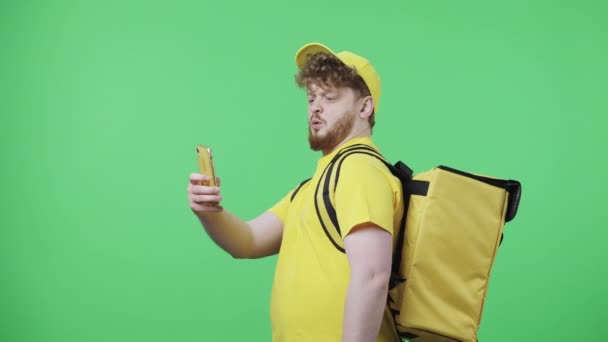 Portré fiatal férfiakról, akik szelfit készítenek mobilon, aztán képeket néznek. Vörös férfi sárga futár egyenruhában, termo táskával, zöld vásznon pózol. Közelről. Lassú mozgás kész 59.97fps. — Stock videók